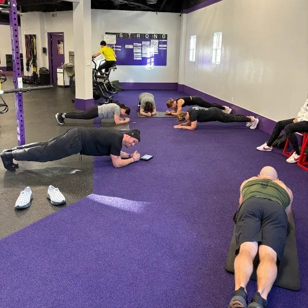 Group of people performing plank exercises together during a fitness training session in a gym